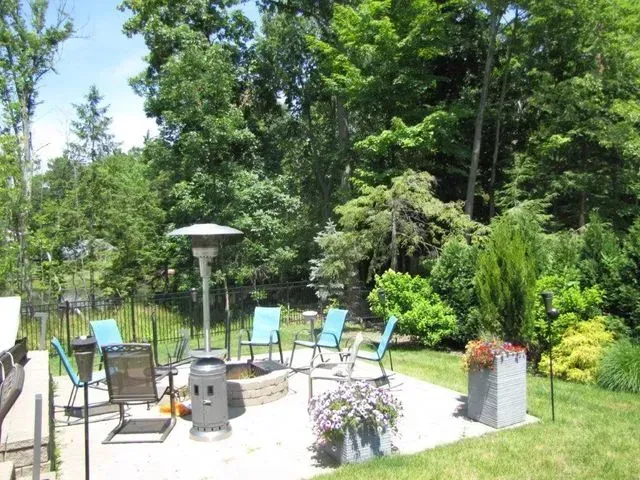 Patio with metal chairs and fire pit, surrounded by lush green trees and shrubs