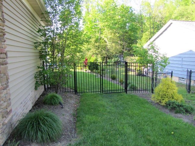 Narrow backyard with green lawn, black metal gate, shrubs, and houses on either side.