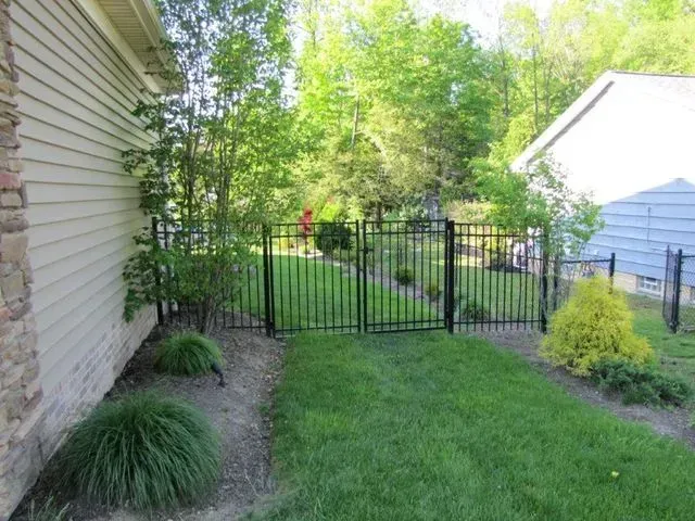 Backyard lawn with black metal gate, flower beds, and a white shed beside a house
