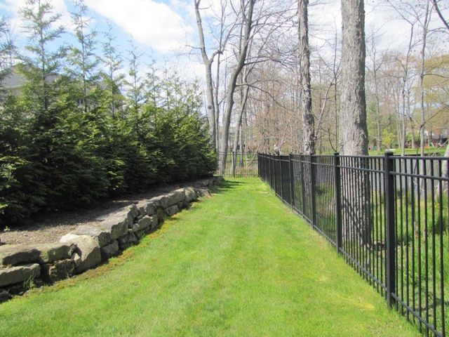 Grassy path beside stone retaining wall and black metal fence in a wooded park