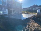 Sunlit backyard with a house, wet patio, and a garden hose on a paved driveway