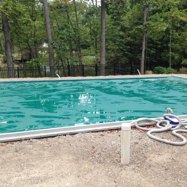 Outdoor swimming pool with turquoise water beside a gravel path and coiled hose, trees in the background