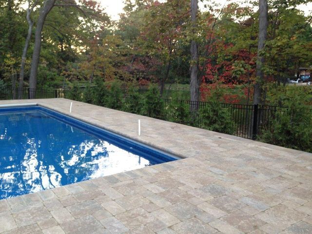 Backyard swimming pool with blue water beside a stone patio and trees