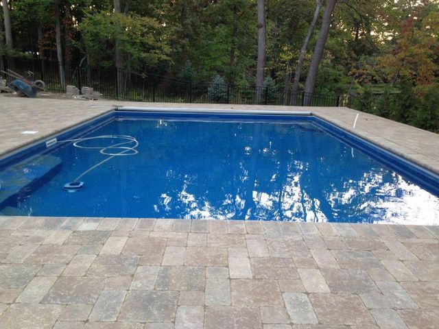 Blue backyard swimming pool with stone deck and surrounding trees