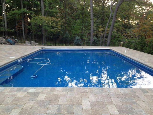 Backyard swimming pool with blue water, stone deck, and trees in the background