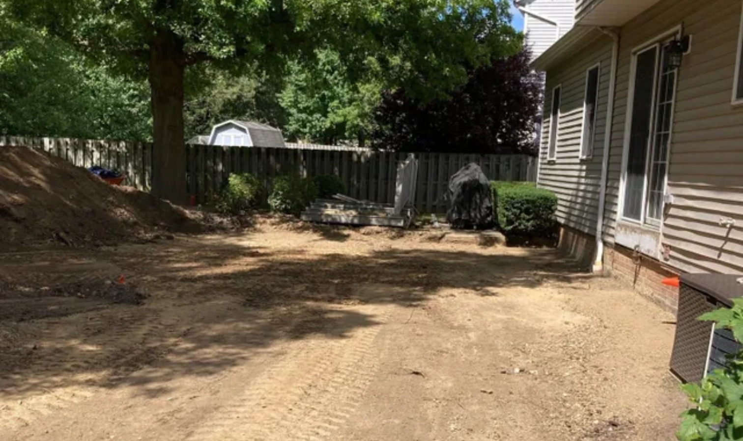 Backyard with bare dirt ground, trees, fence, and house siding on the right