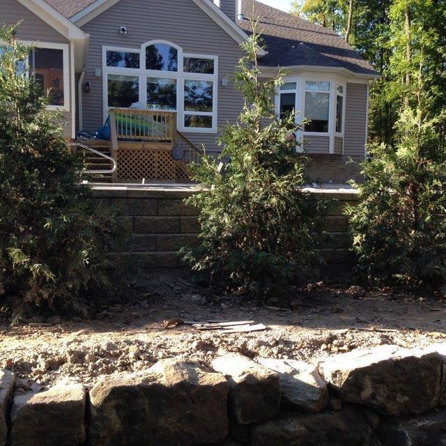 House with large windows and stone retaining wall overlooking a landscaped slope