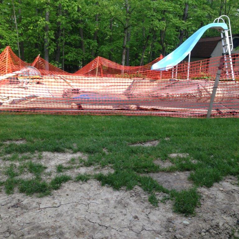Closed playground with orange safety fence and blue slide on a grassy, wooded site