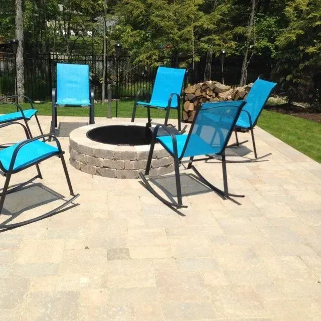 Blue chairs around a stone fire pit on a sunny patio in a backyard