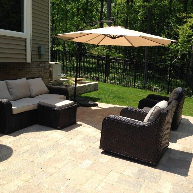 Outdoor patio with wicker seating and a beige umbrella beside a house and black fence.