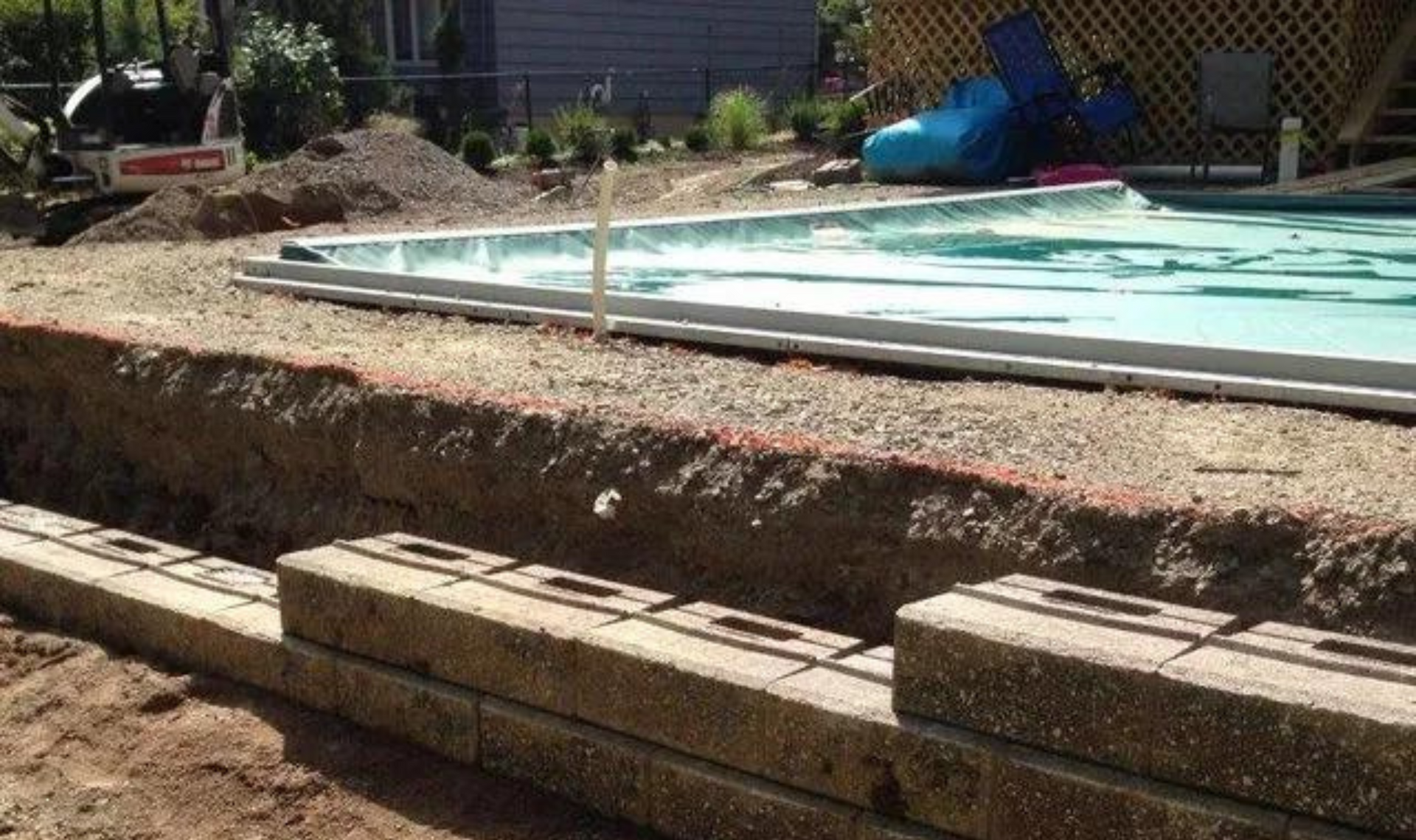 Backyard pool with a large dirt excavation and stacked wood planks in the foreground
