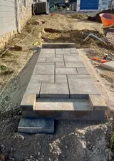 Construction site with newly laid gray paver walkway over dirt, unfinished at the edges