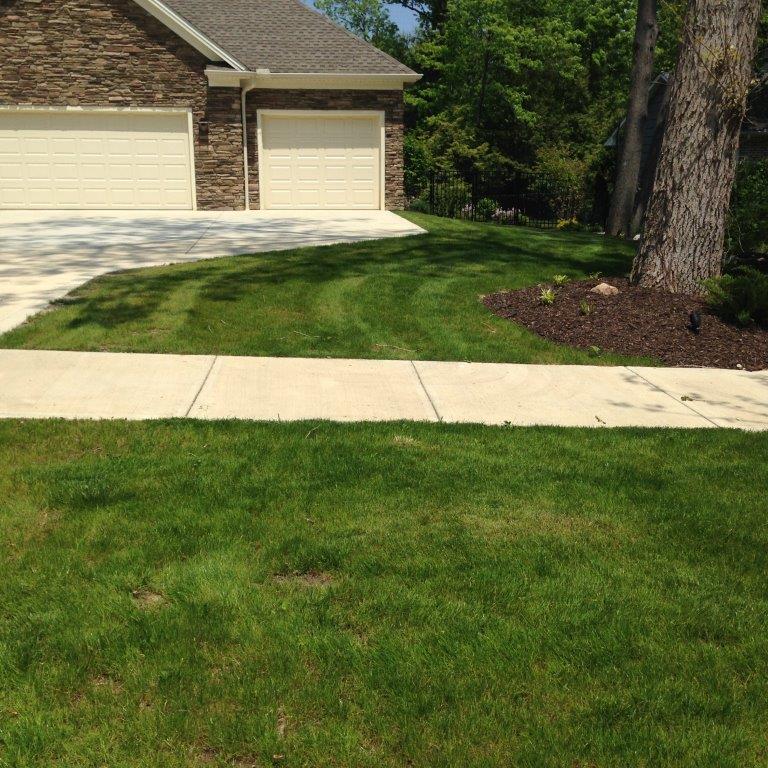 Suburban front yard with green lawn, sidewalk, and brick house with garage doors