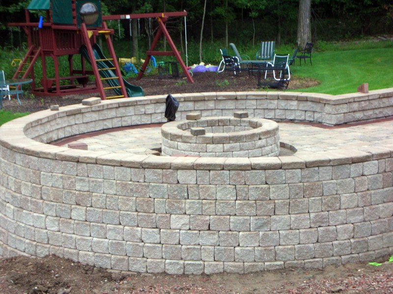 Stone outdoor fountain in a park with a black cat sitting on the circular ledge