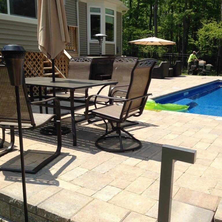 Patio with black metal chairs and table beside a blue swimming pool and beige house.