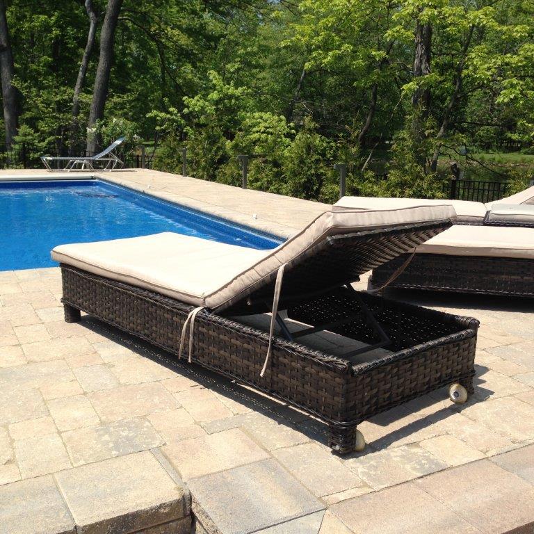 Poolside wicker chaise lounge with open canopy on a stone patio beside a blue swimming pool