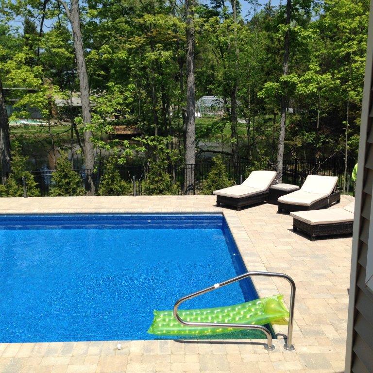 Backyard pool with lounge chairs and a green pool lift beside the blue water