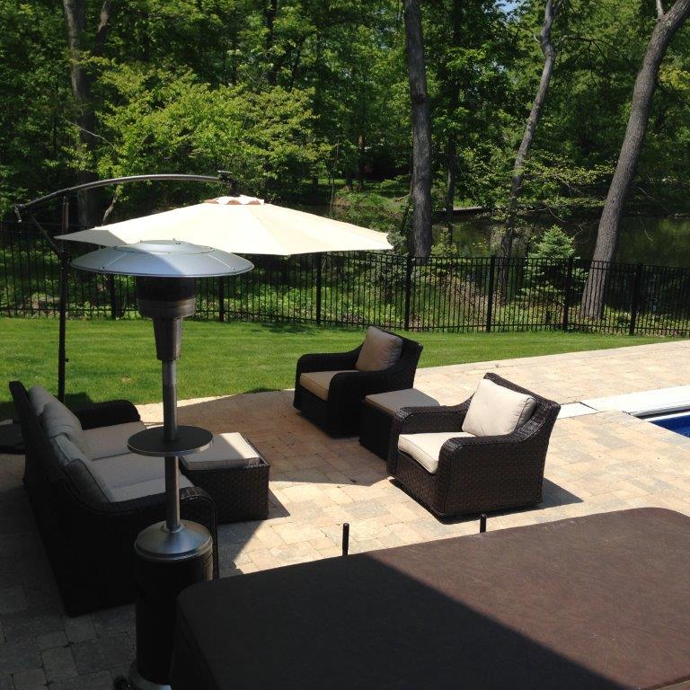 Patio with outdoor chairs, table umbrellas, and a pool beside a wooded backyard