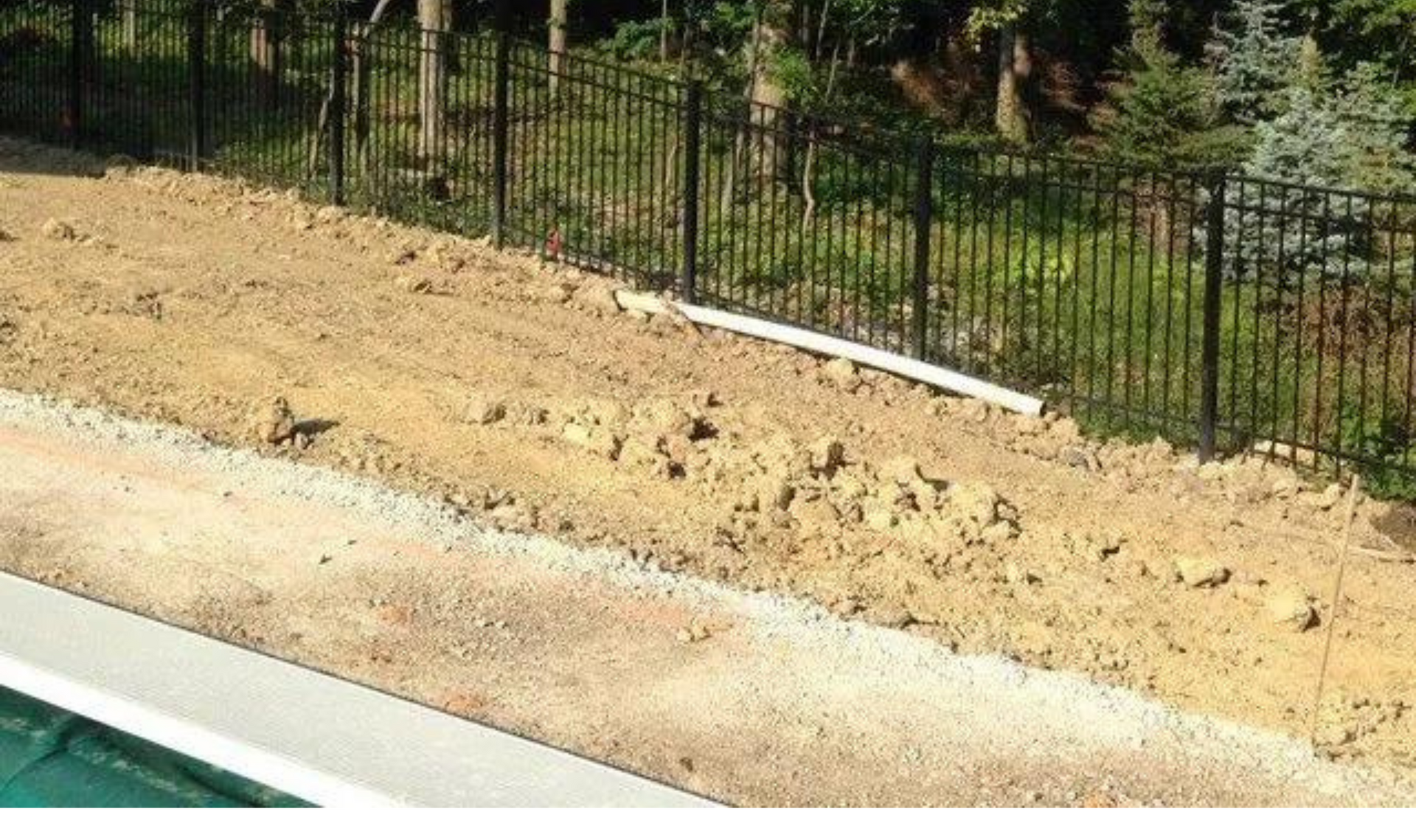 Bare soil beside a white curb and black metal fence, with a pool edge in the foreground.