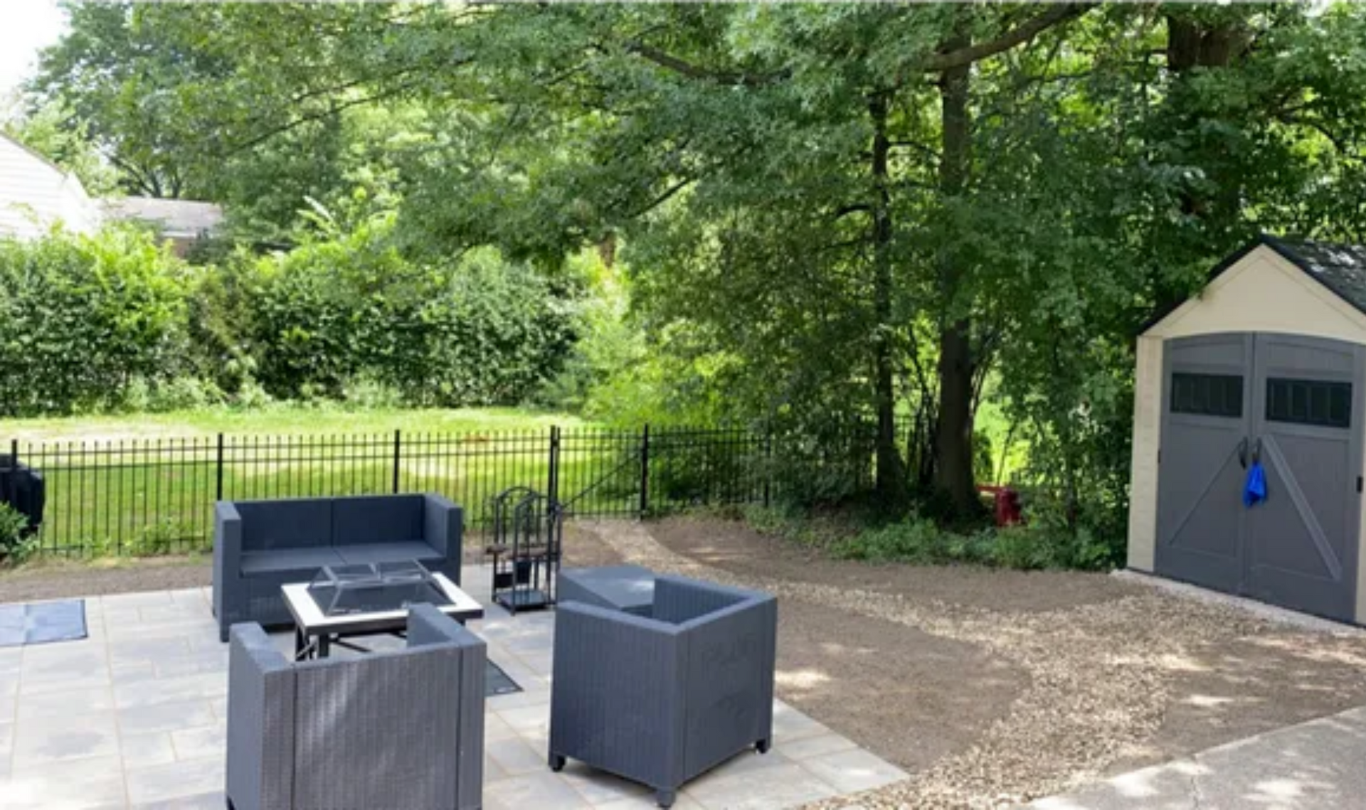 Patio seating area with gray outdoor chairs, a fire pit, and a beige storage shed beside a fenced yard.
