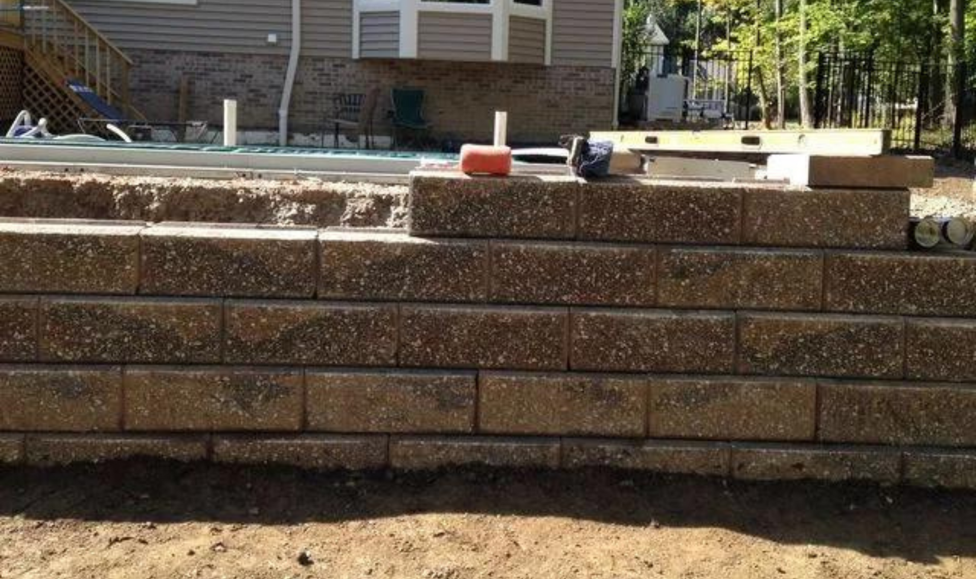 Stacked retaining wall blocks in a backyard, with tools and a house in the background.