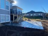 Backyard deck and patio beside a blue house, with a sloped yard and neighboring homes beyond