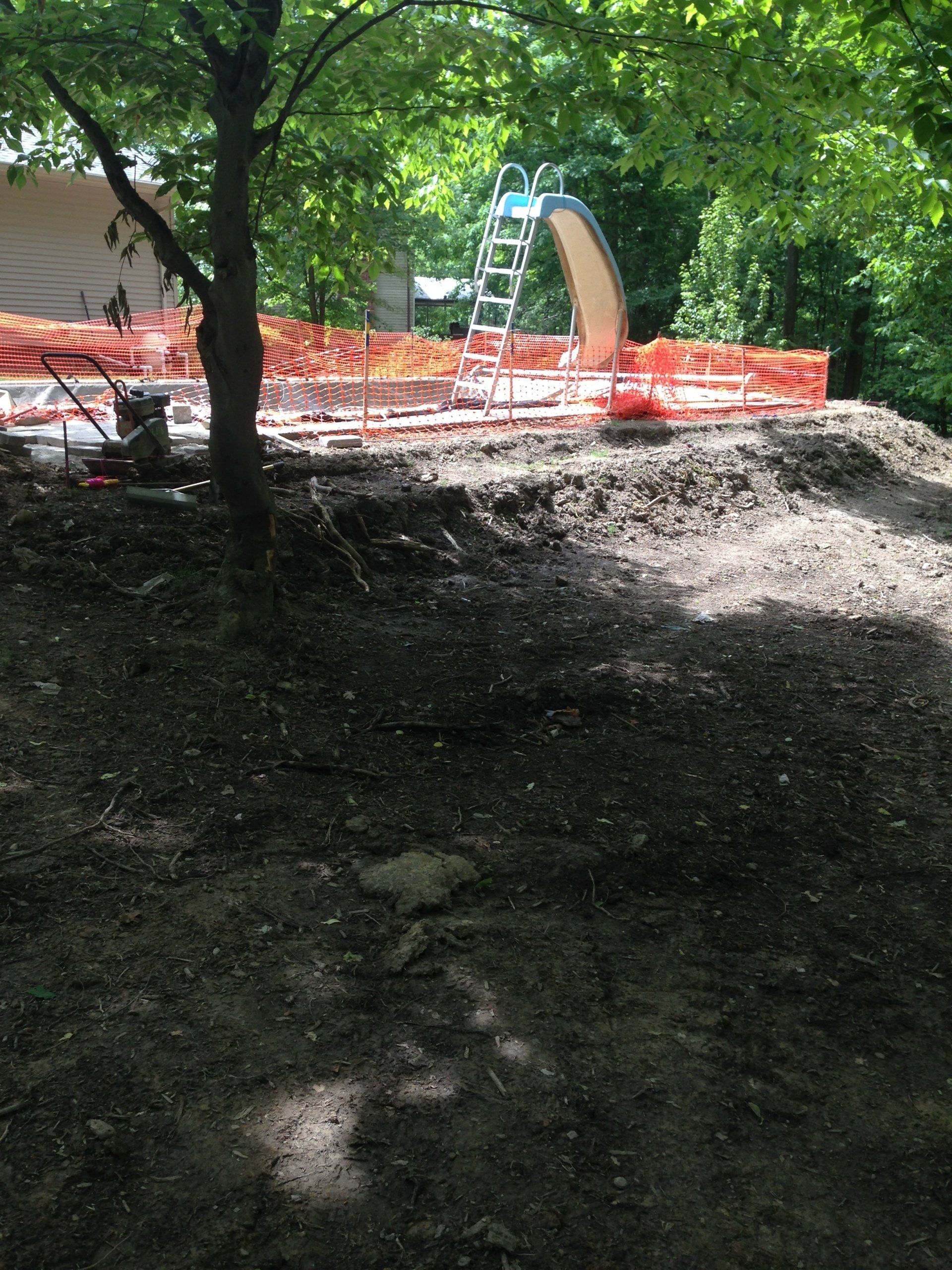Construction site with orange safety fencing and blue ladder slide in a shaded wooded area
