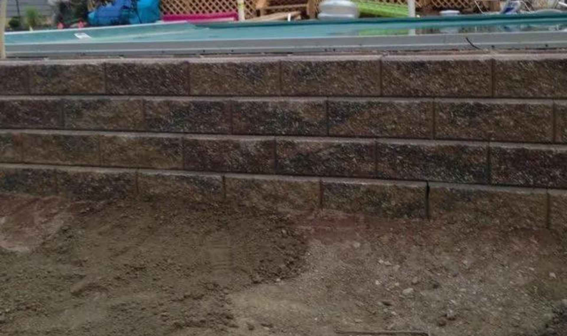 Stone steps beside a dirt path in an outdoor garden area with a blue railing and potted plants.
