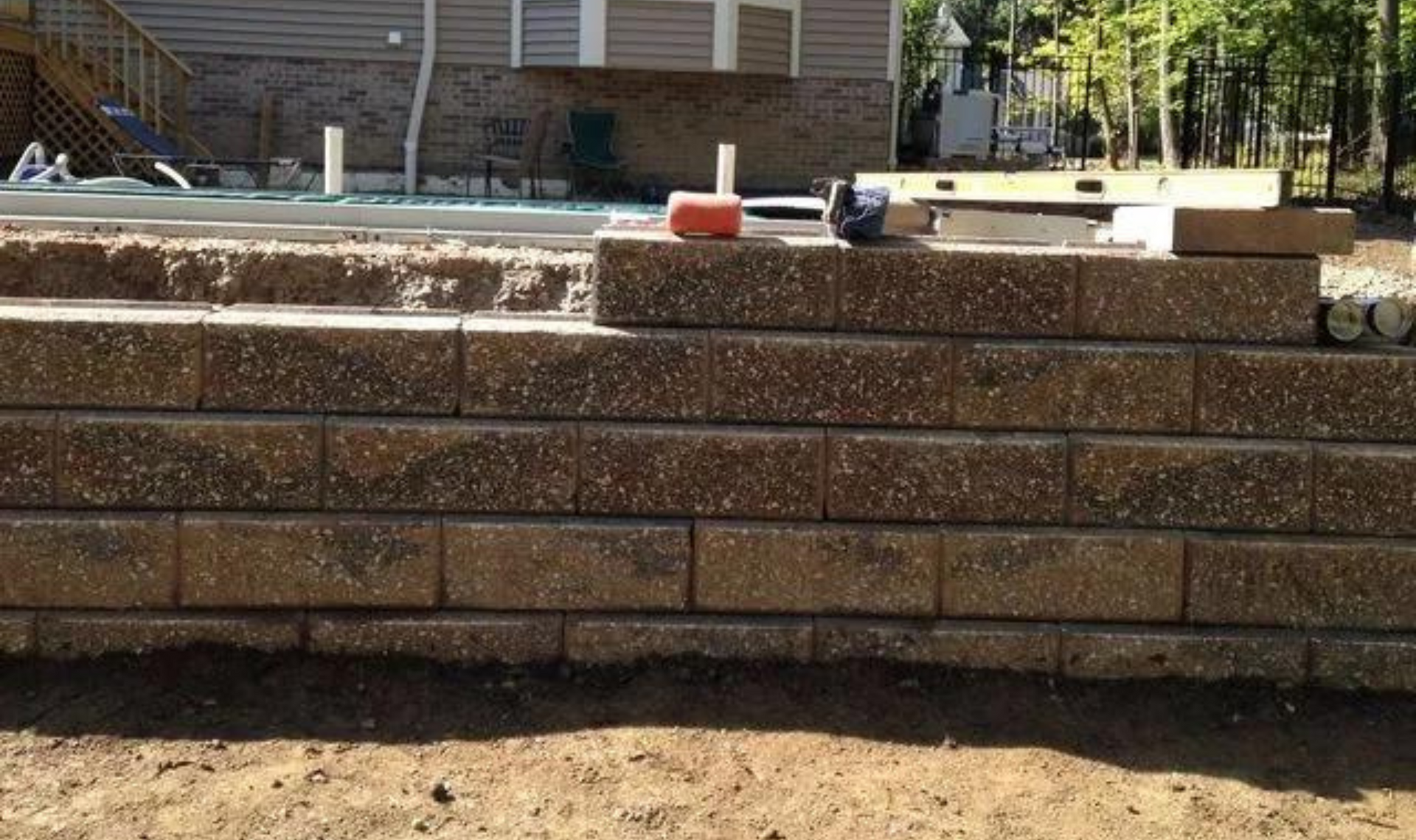 Stone retaining wall in a backyard with a patio and pool in the background.