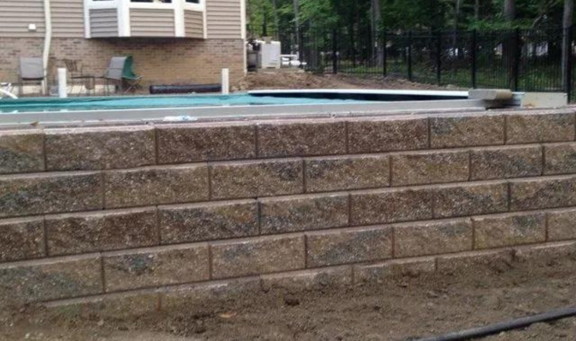 Raised stone retaining wall in front of an above-ground pool by a house