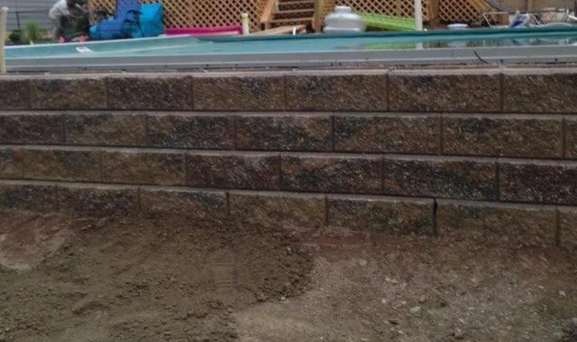 Stone retaining wall with a dirt slope and a pool edge visible above it