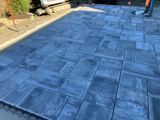 Blue stamped concrete patio or driveway in sunlight with a person’s legs visible at the edge