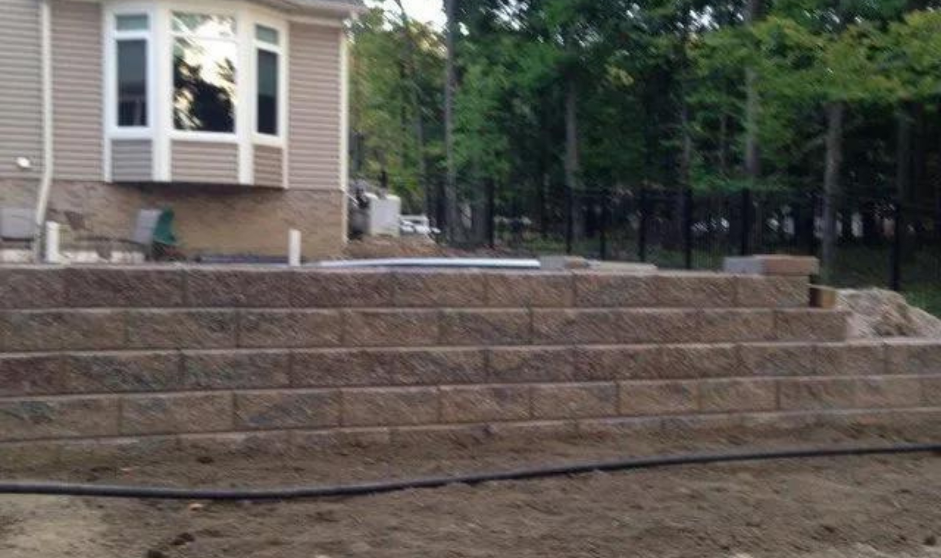 Stone retaining wall and stepped patio leading up to a house with a wooded backyard.