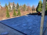 Rooftop under construction with dark roofing in a wooded area, seen from a deck or porch.