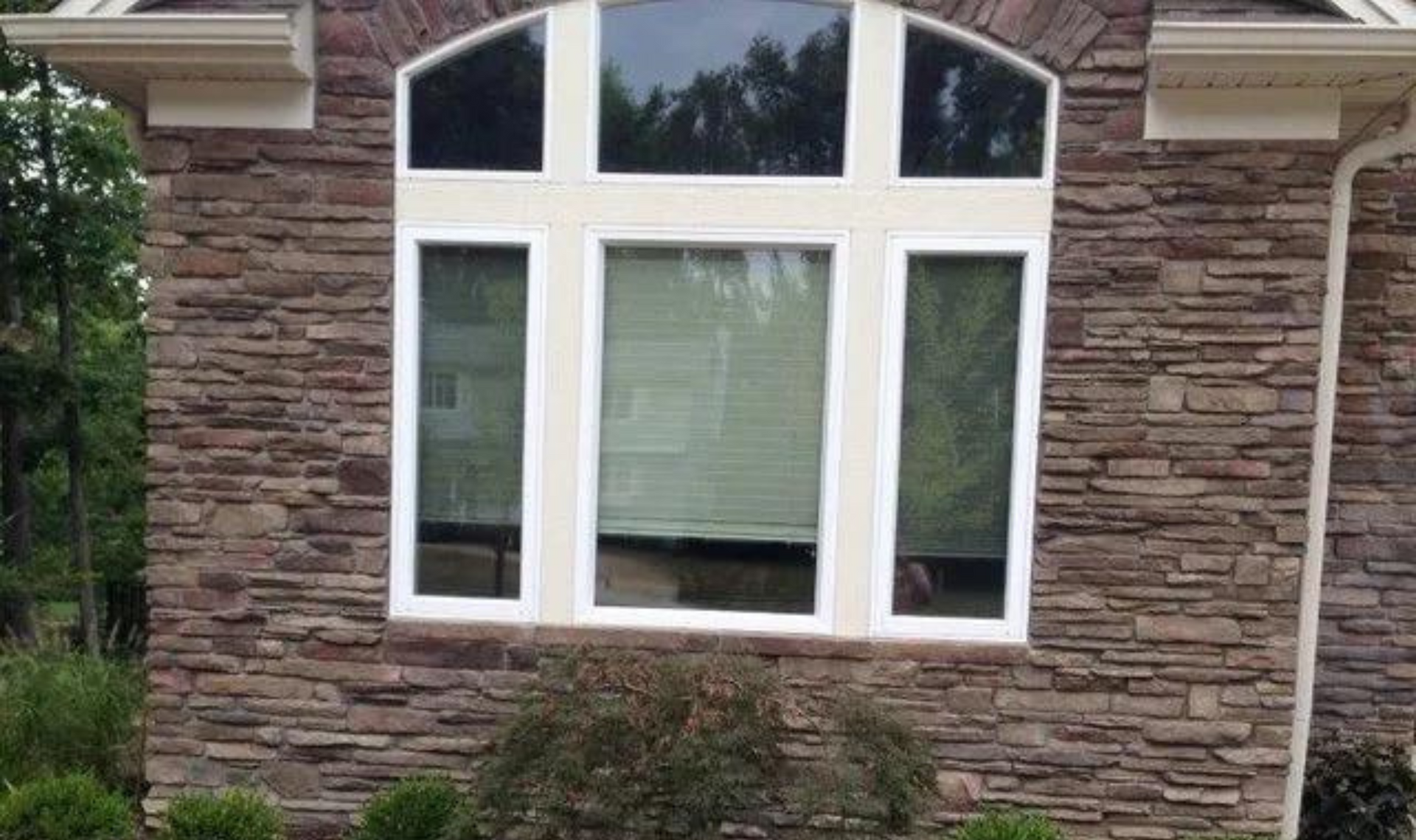 Three white-framed windows in a stone house wall, with an arched window above the center.