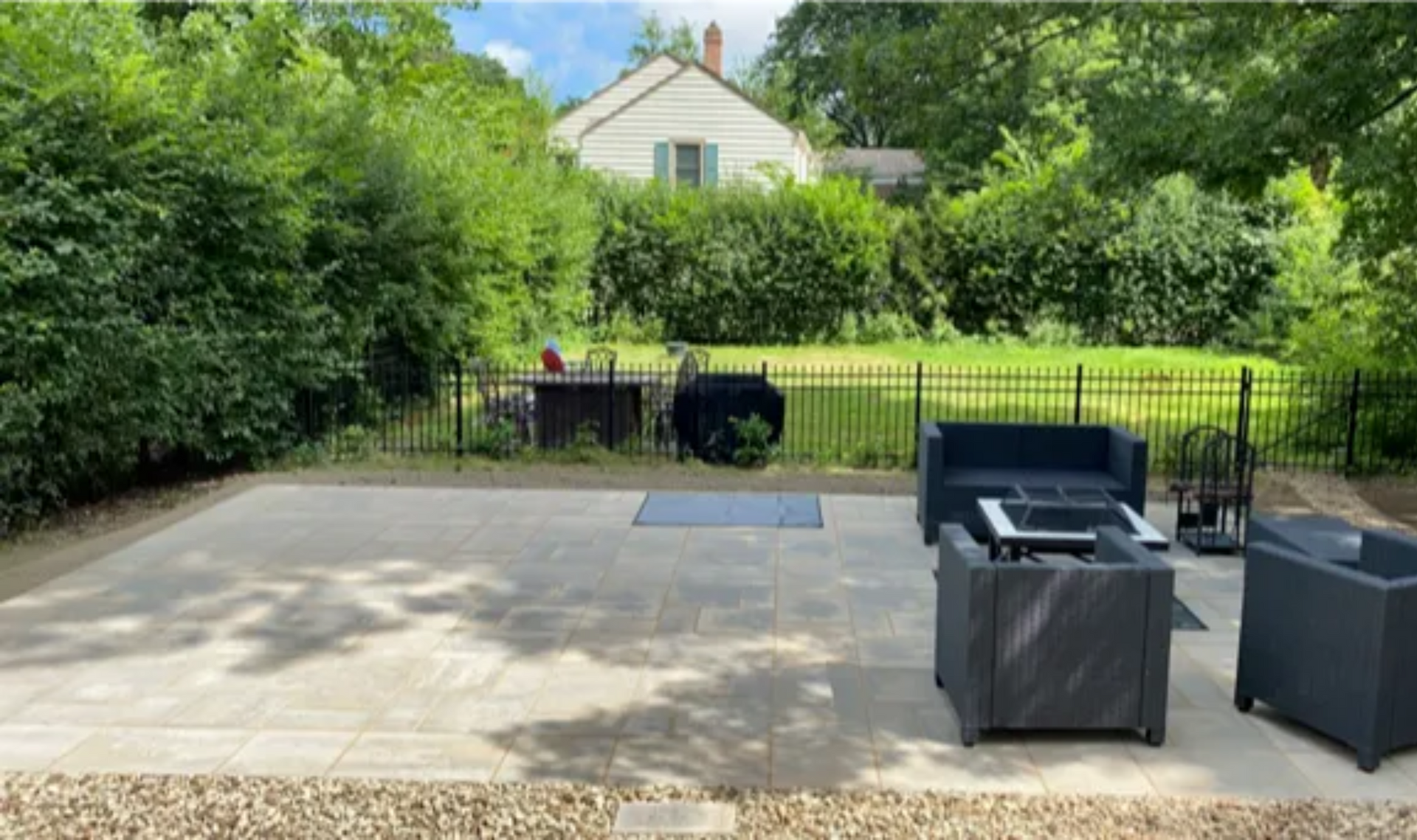 Patio with black wicker chairs, gravel edge, and lush green hedges in front of a house and fence
