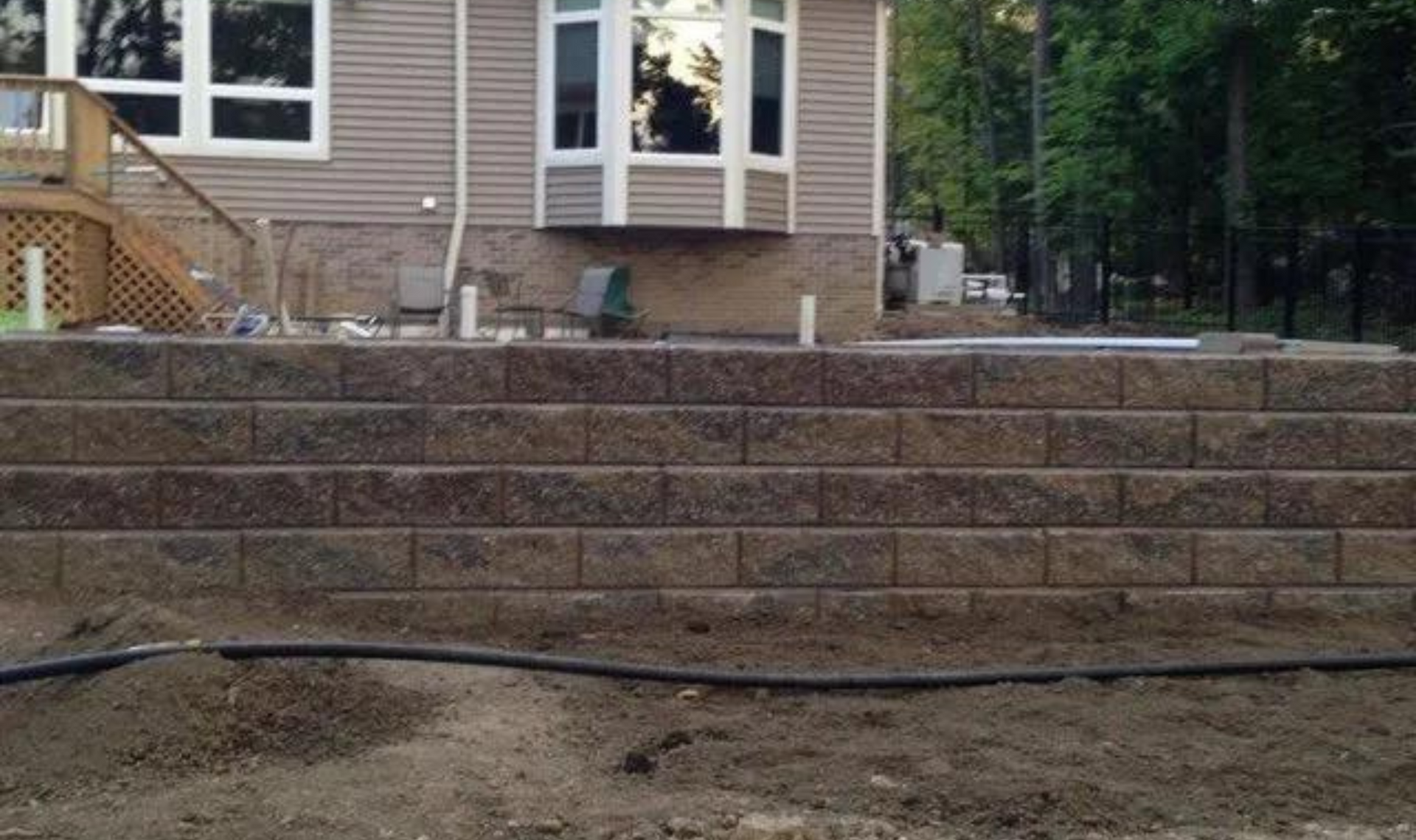 Backyard retaining wall with wide stone steps leading up to a house deck