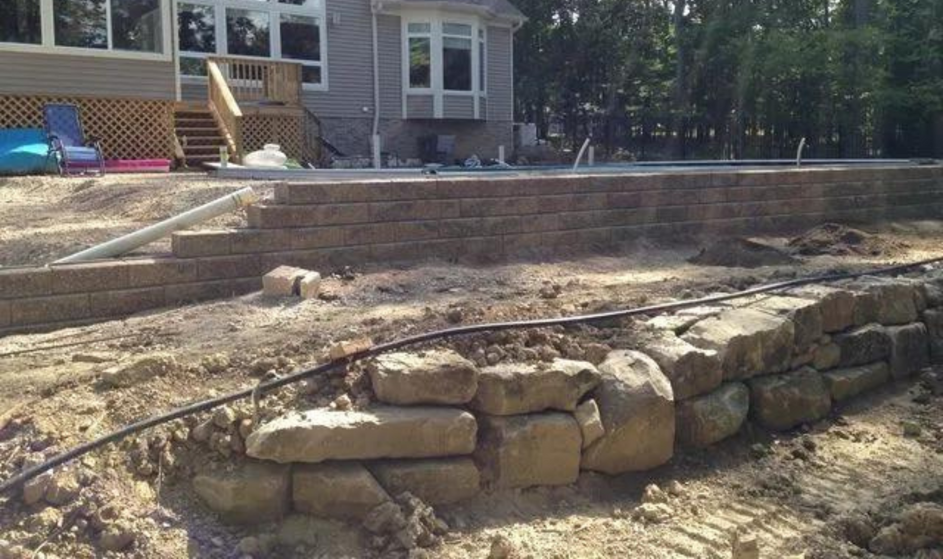 Stone retaining wall in a backyard under construction beside a house and patio