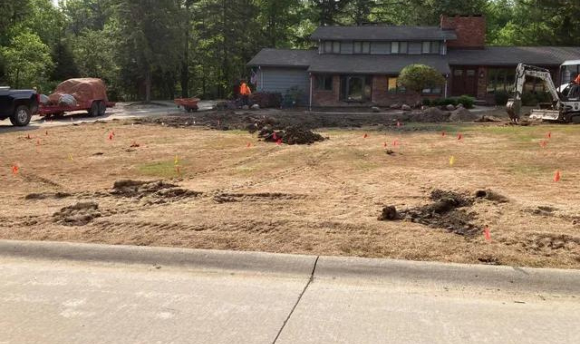 Front yard under construction with dirt patches, orange markers, and a house in the background.