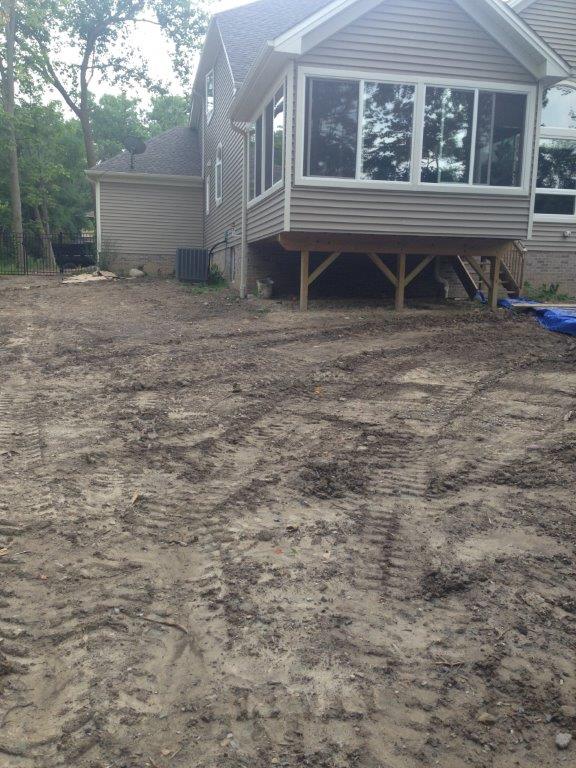 Backyard with a raised house on stilts and a muddy, uneven dirt lot in front