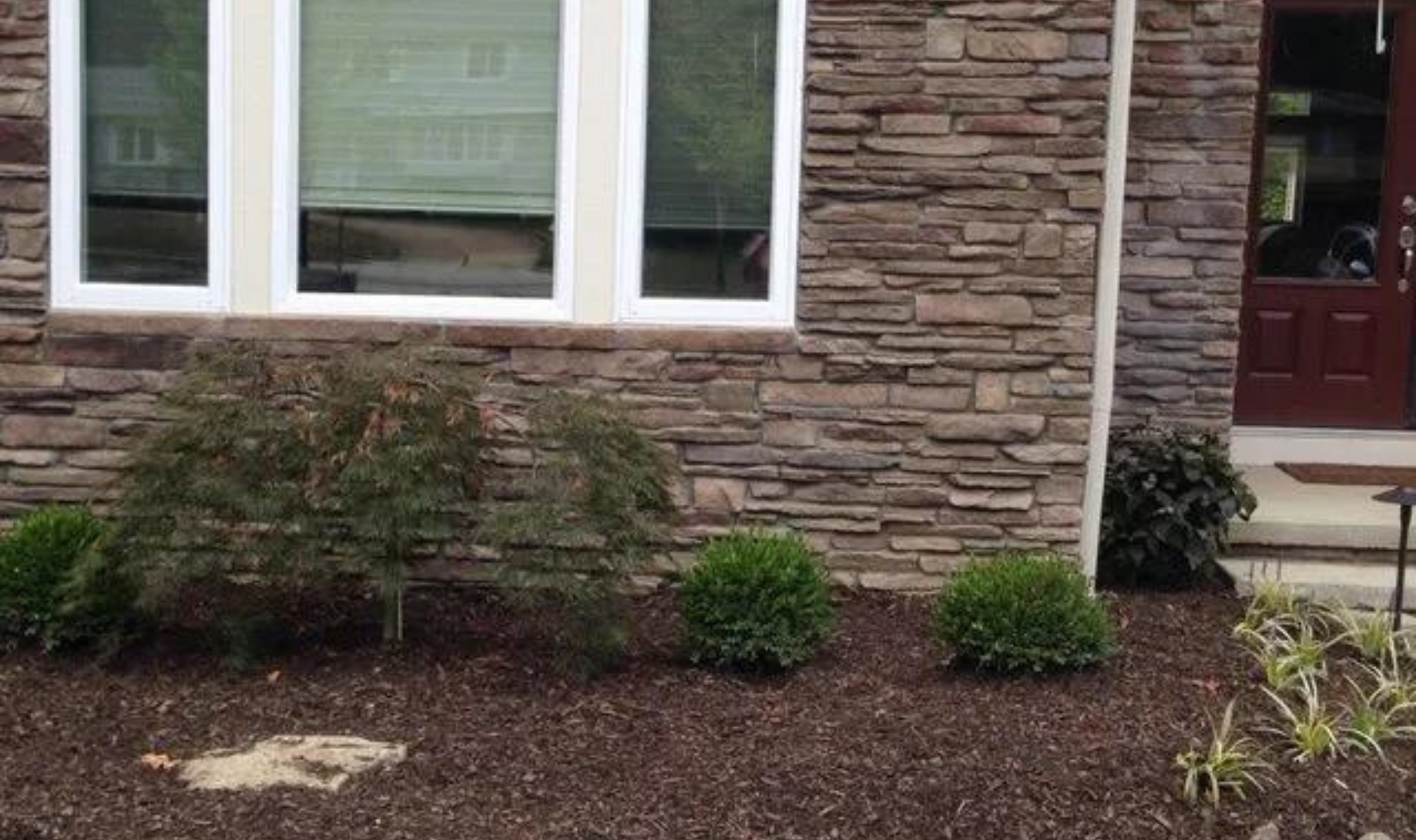 Stone house exterior with windows, shrubs, and mulch landscaping