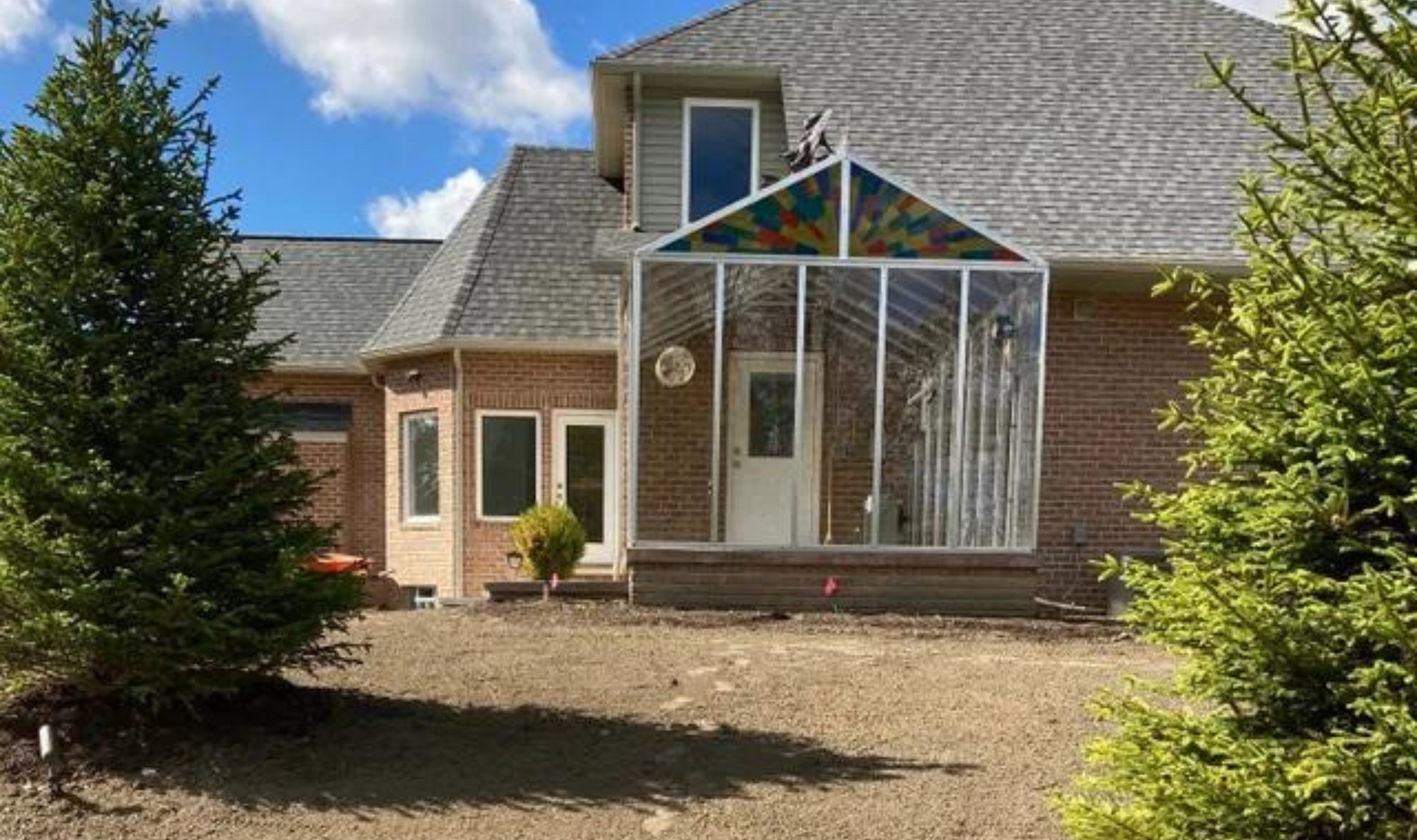 Suburban house with a small glass-enclosed front porch and evergreen trees in the yard