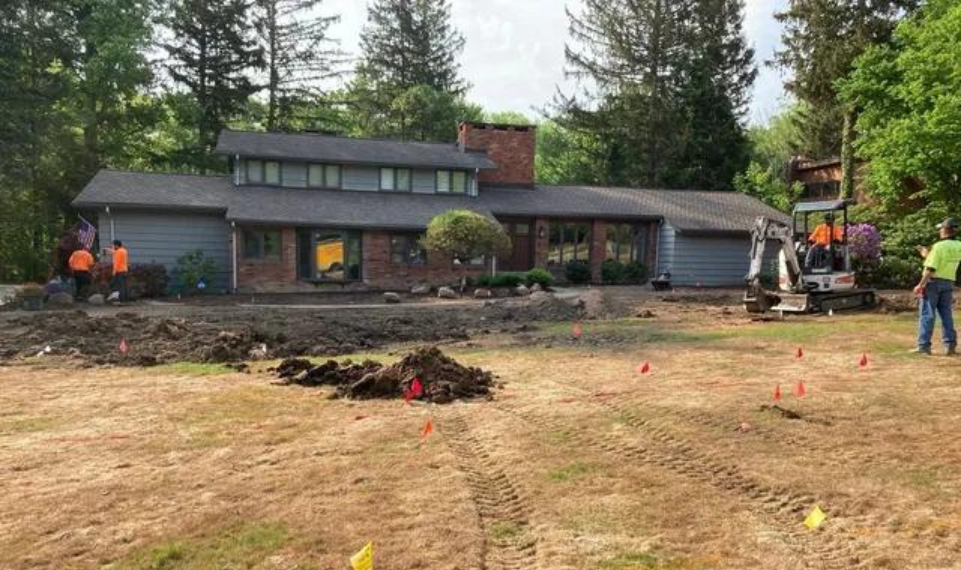 House and workers beside a freshly disturbed yard with dirt piles and equipment, likely a landscaping or repair site