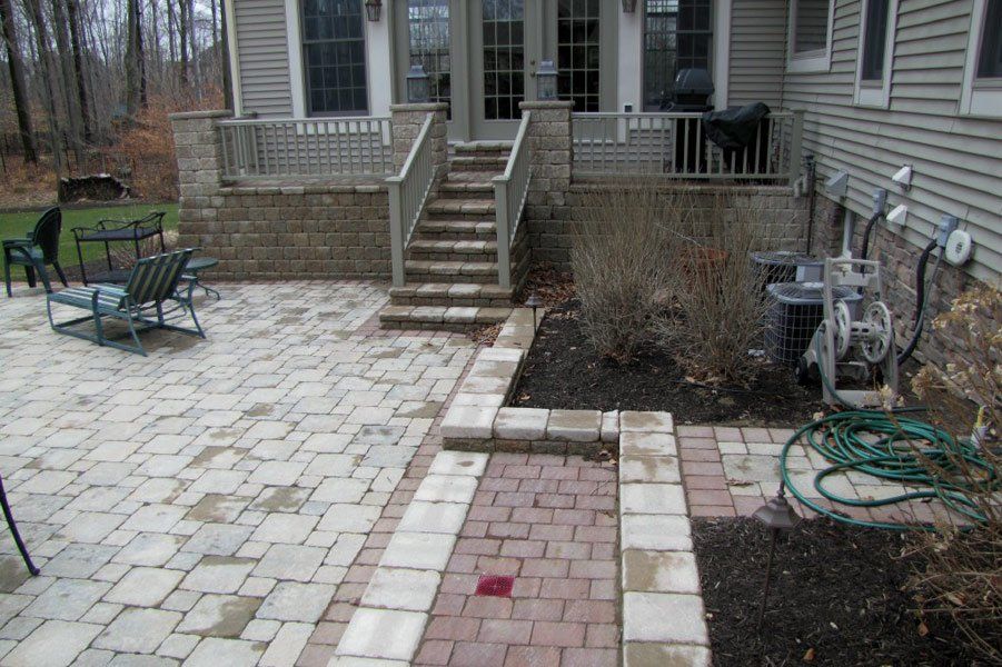 Brick patio and steps leading to a house deck, with outdoor chairs and a coiled green hose.