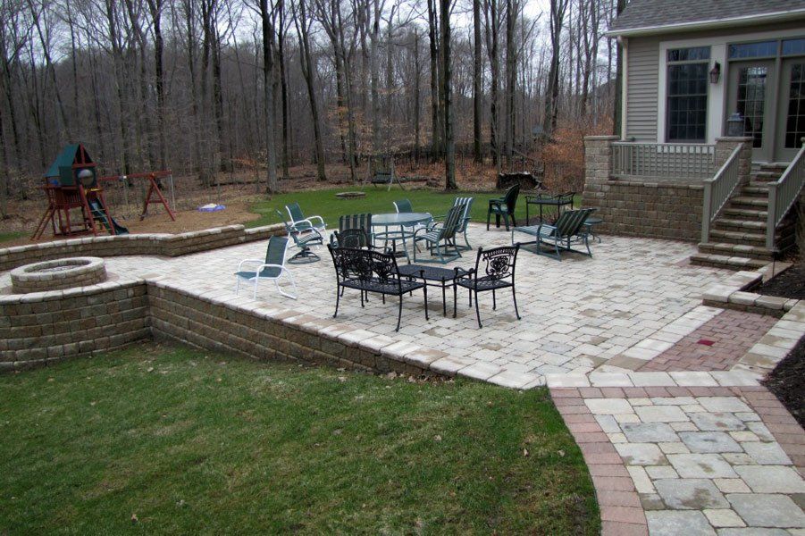 Patio with outdoor dining set, stone pavers, and steps beside a house, backed by a wooded yard