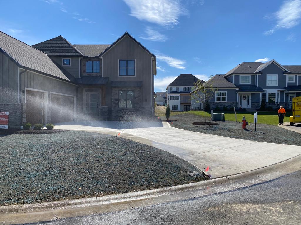 New homes under construction with gravel driveway, spraying water, and blue sky on a sunny day