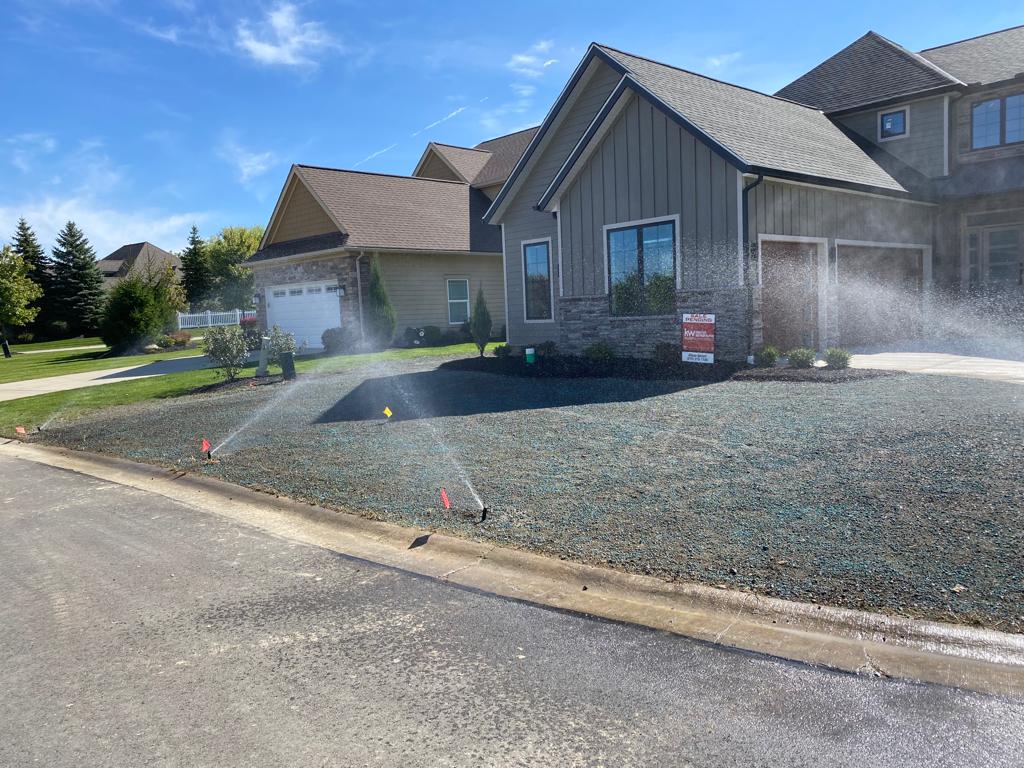 Suburban houses with gravel front yards being watered by sprinklers on a sunny day