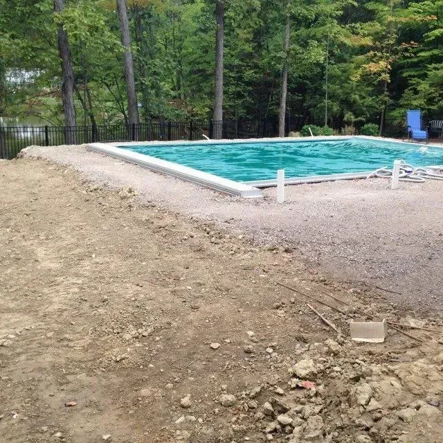 Outdoor swimming pool with turquoise water beside a dirt lot and trees