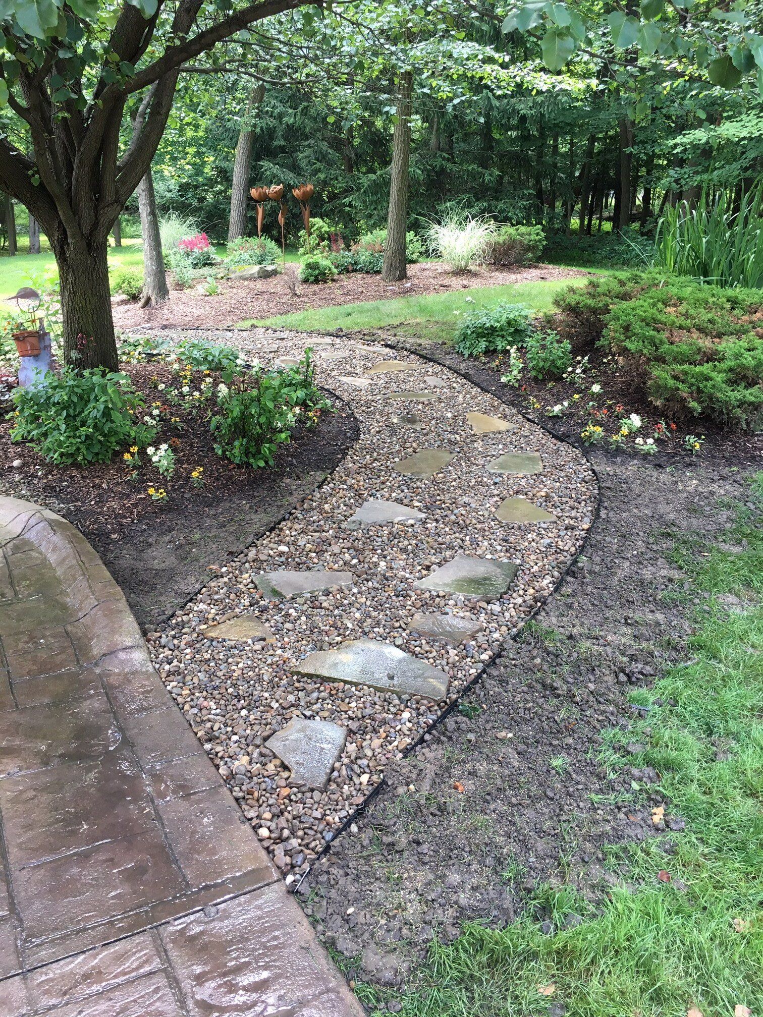 Curved gravel garden path bordered by brick and flower beds under trees