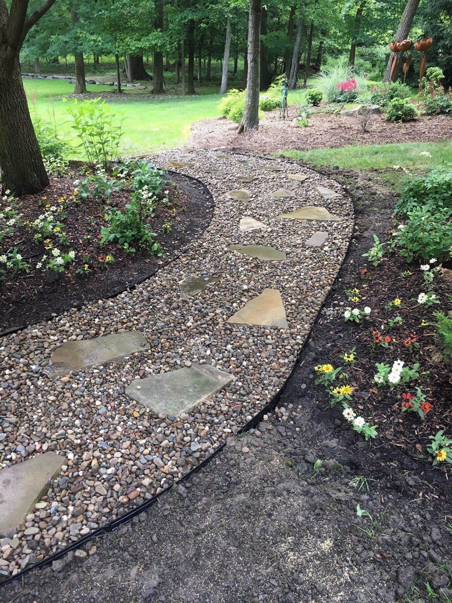 Curved stone garden path through mulch and flower beds in a green park.